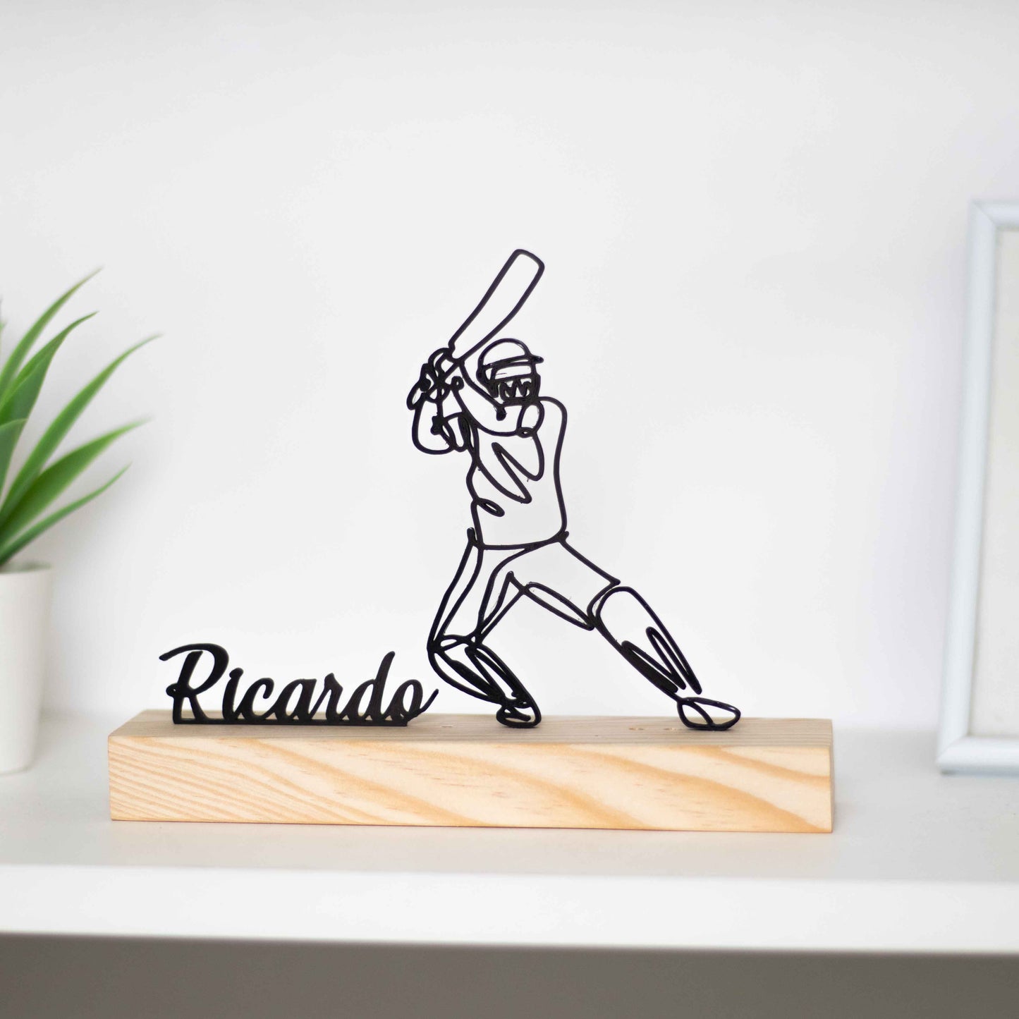 Escultura troféu de críquete com base de madeira, representando um jogador em ação. Ideal como prémio de competição, presente para atletas ou decoração temática. Personalizável com um nome à escolha, perfeito para fãs do críquete.