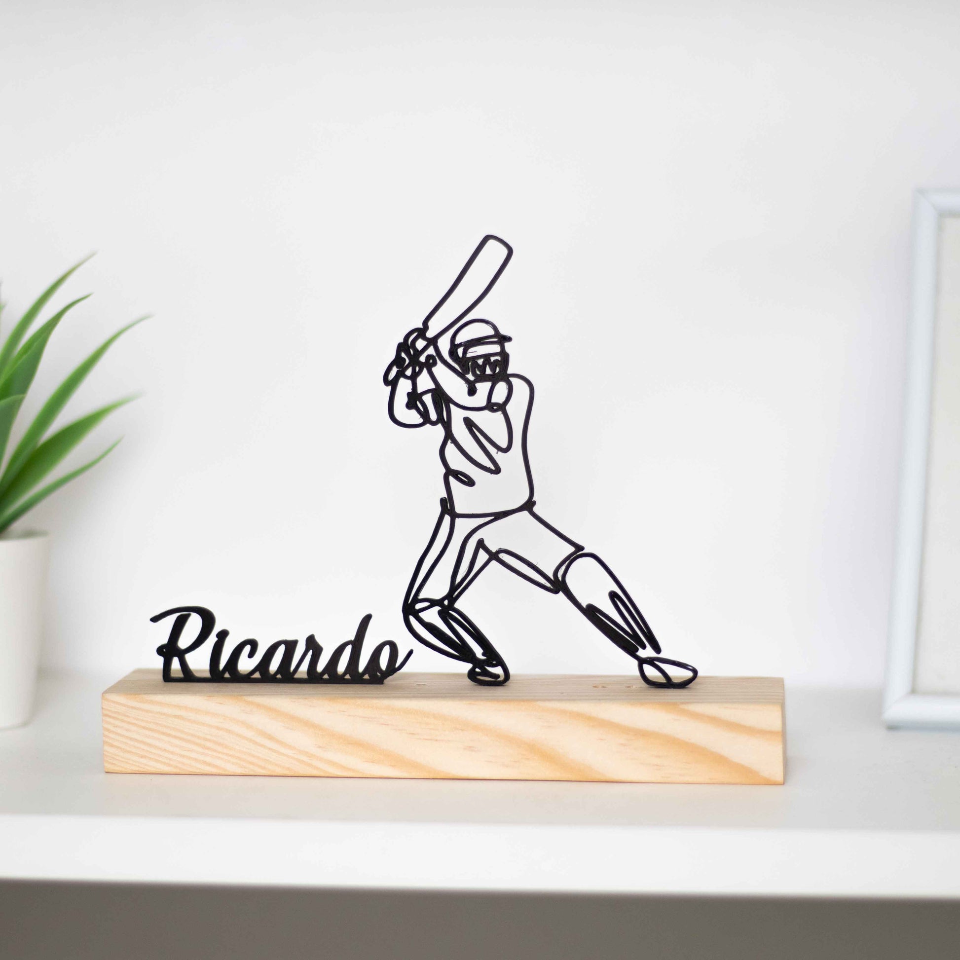 Escultura troféu de críquete com base de madeira, representando um jogador em ação. Ideal como prémio de competição, presente para atletas ou decoração temática. Personalizável com um nome à escolha, perfeito para fãs do críquete.