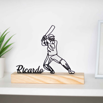 Escultura troféu de críquete com base de madeira, representando um jogador em ação. Ideal como prémio de competição, presente para atletas ou decoração temática. Personalizável com um nome à escolha, perfeito para fãs do críquete.